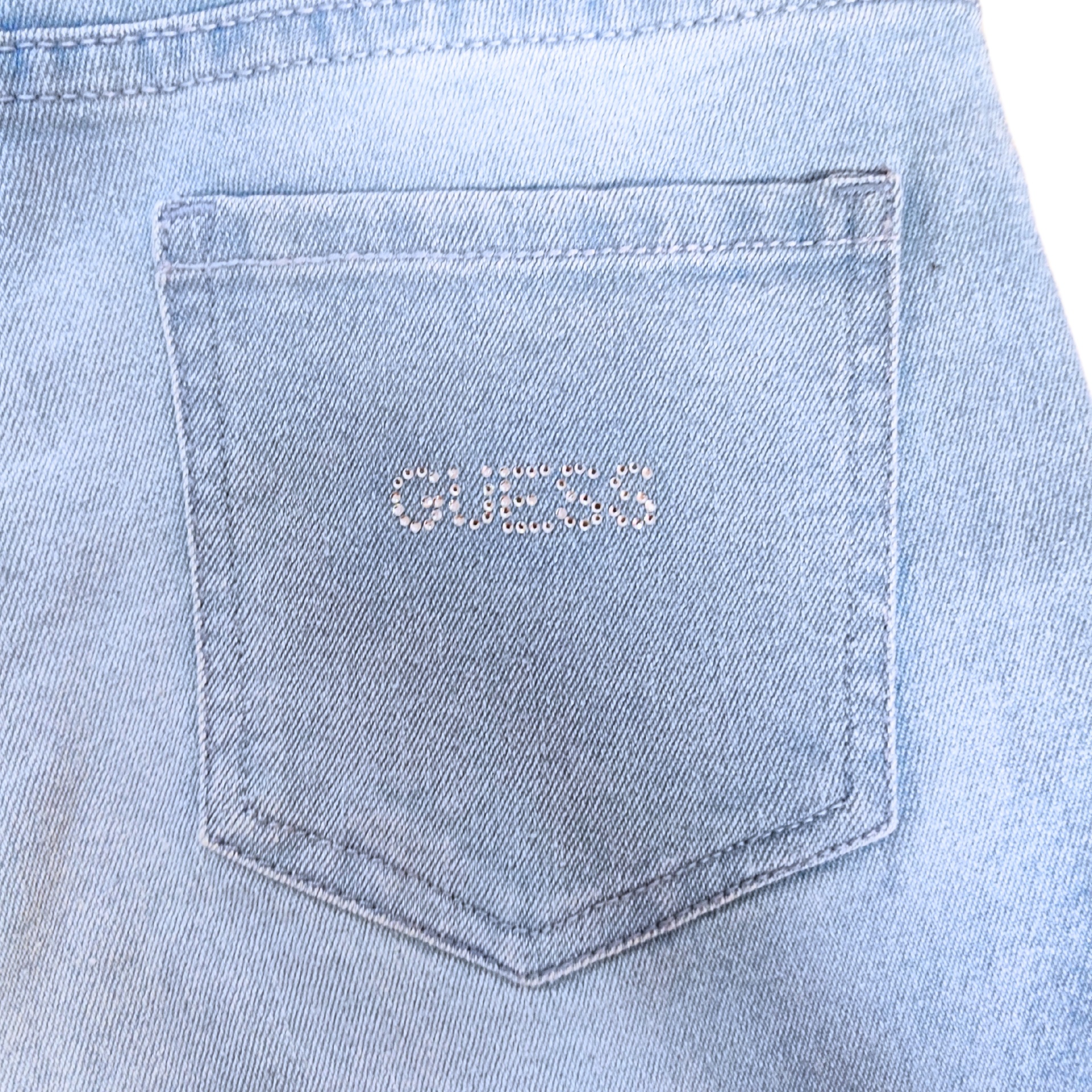 Bolso traseiro de ganga azul clara com a palavra 'GUESS' em brilhantes