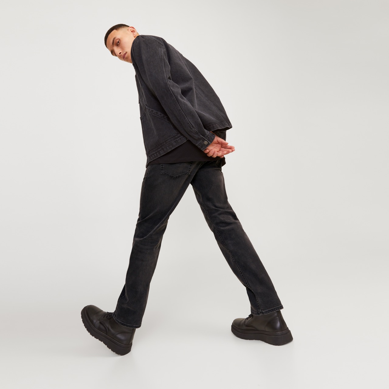 Homem com camisa e calças pretas de denim e sapatos pretos em fundo branco