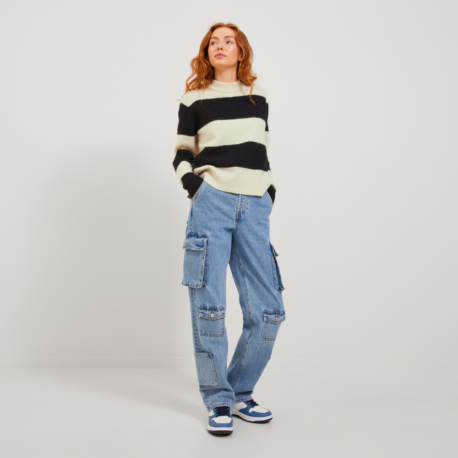 Mulher a usar camisola riscada preto e creme, calças ganga azuis com bolsos e ténis brancos e azuis