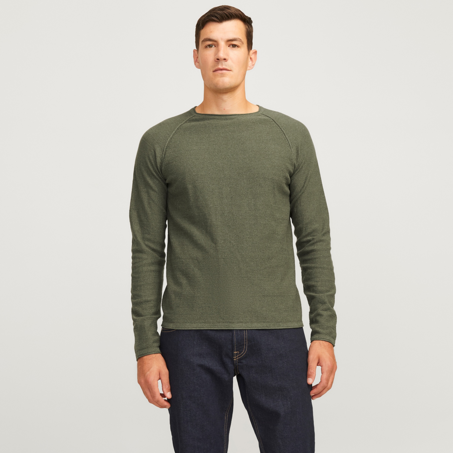 Homem a usar camisola verde-oliva de malha fina com calças de ganga azul escuro