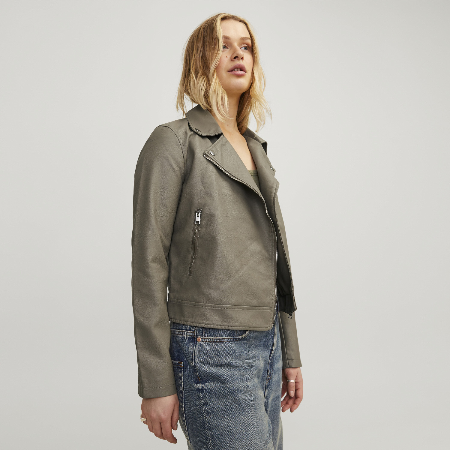 Casaco biker cinzento em pele falsa com fecho e mulher com jeans azuis