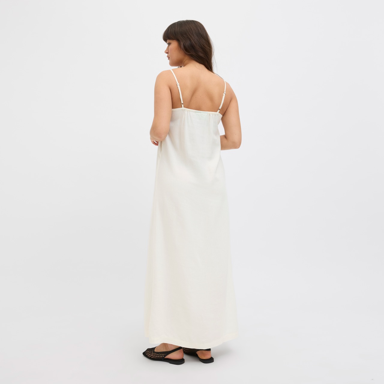 Mulher de costas com vestido branco comprido de alças finas e sapatos pretos