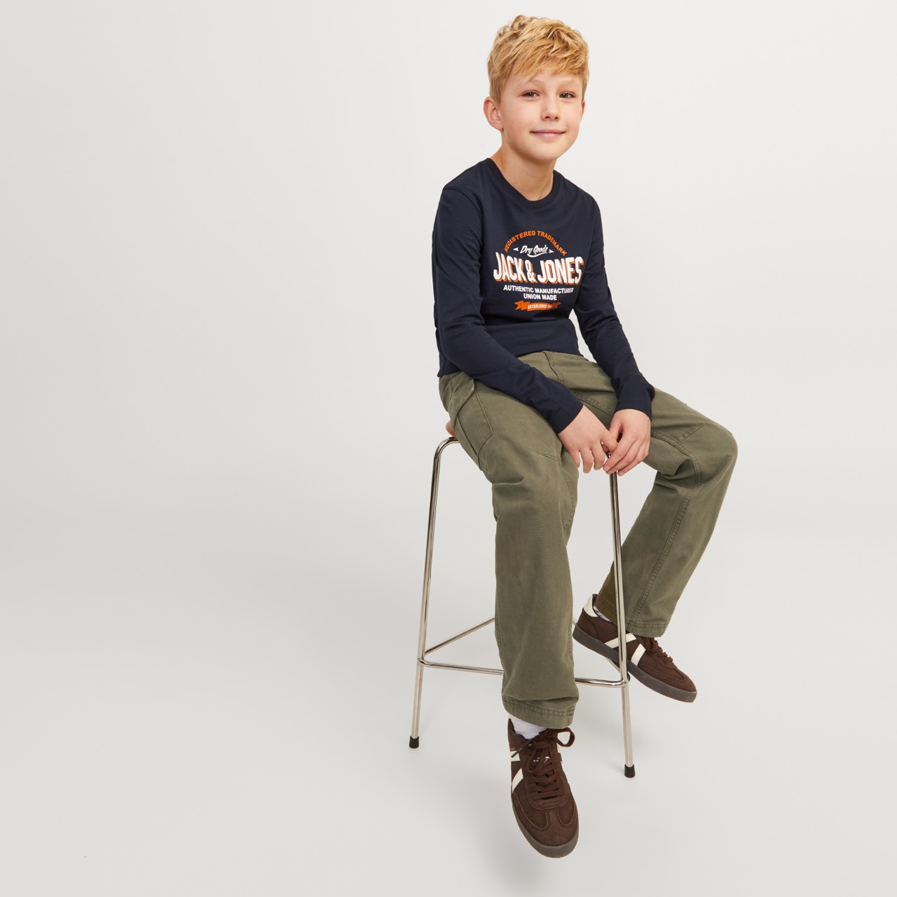 Menino com camisola preta JACK & JONES e calças verdes sentado num banco alto