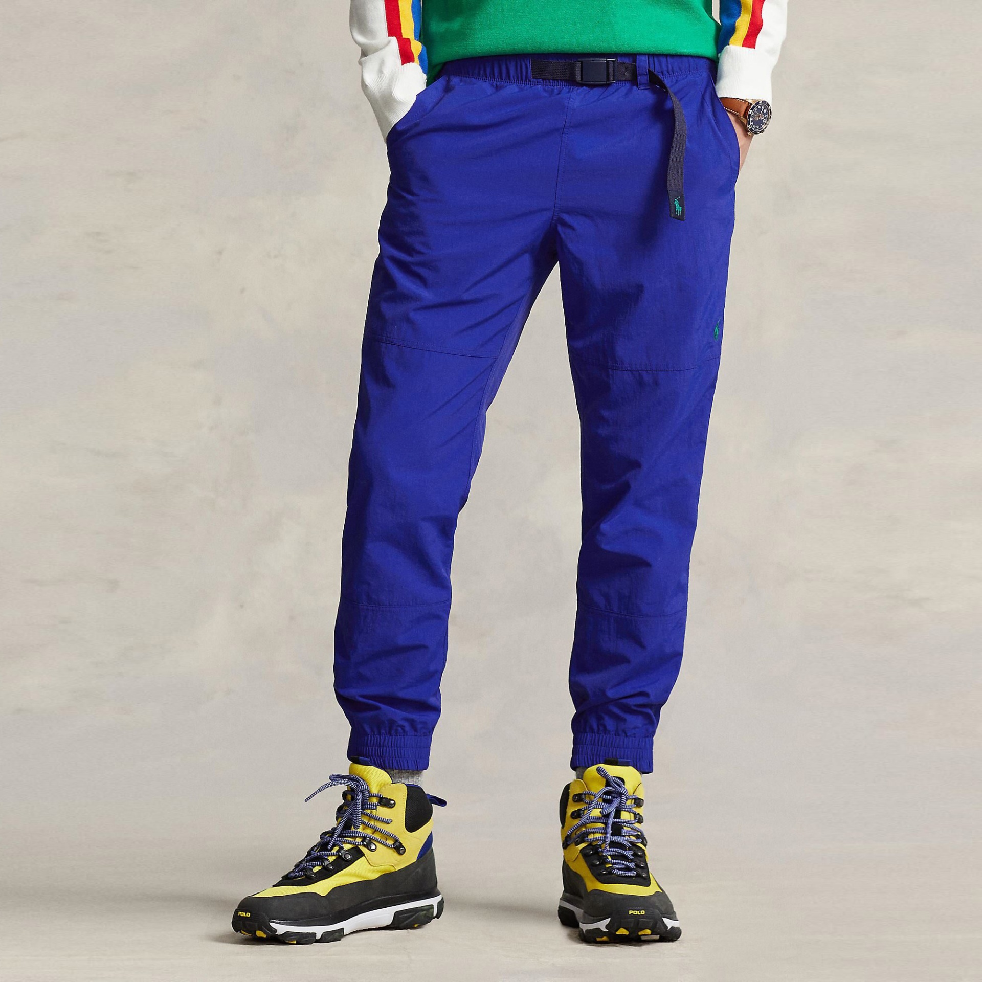 Calças desportivas azuis com cós elástico e cinto ajustável preto e sapatilhas amarelas e pretas.