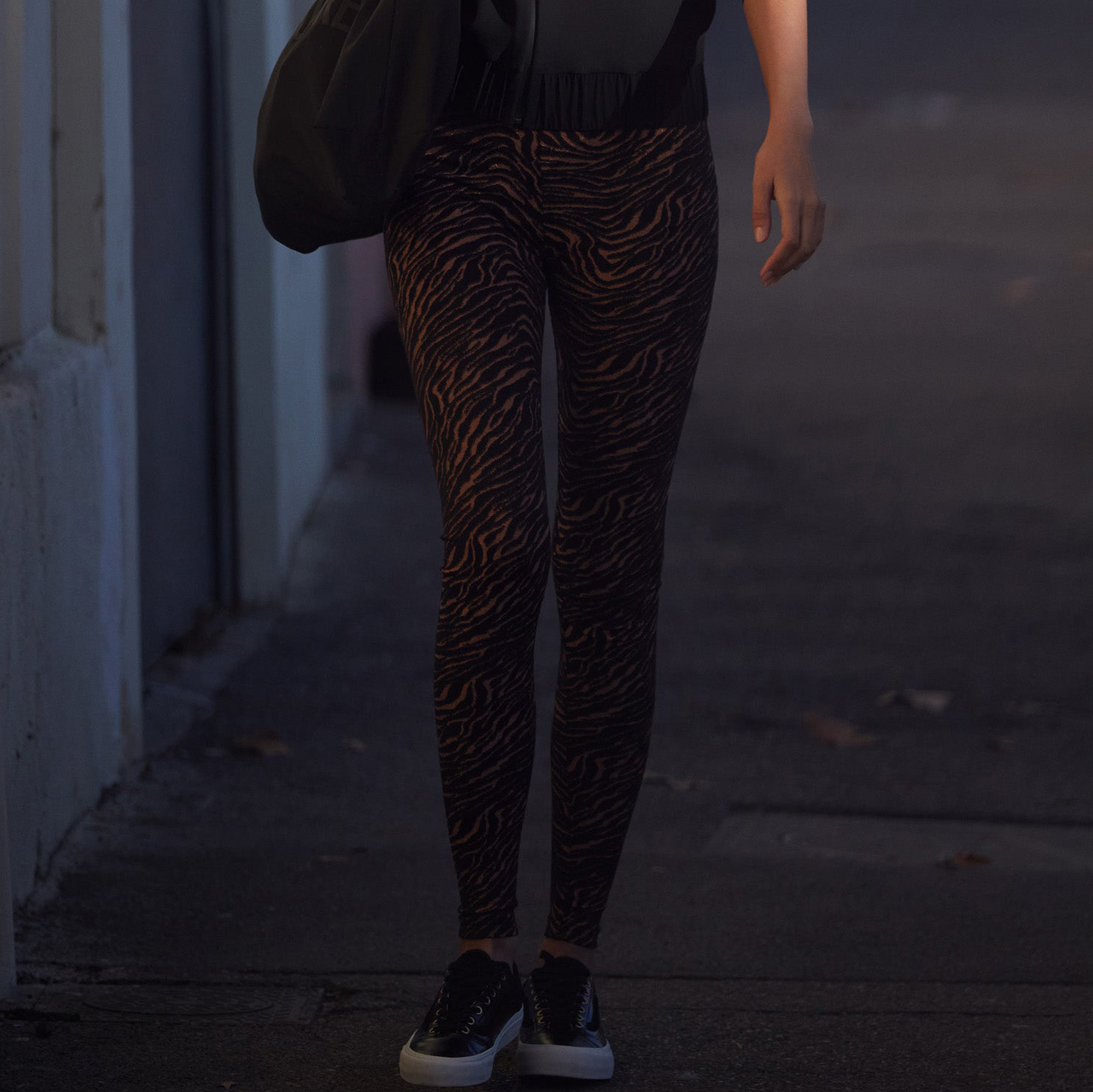 Leggings castanhas e pretas com padrão tipo pele de zebra e ténis pretos nas ruas à noite