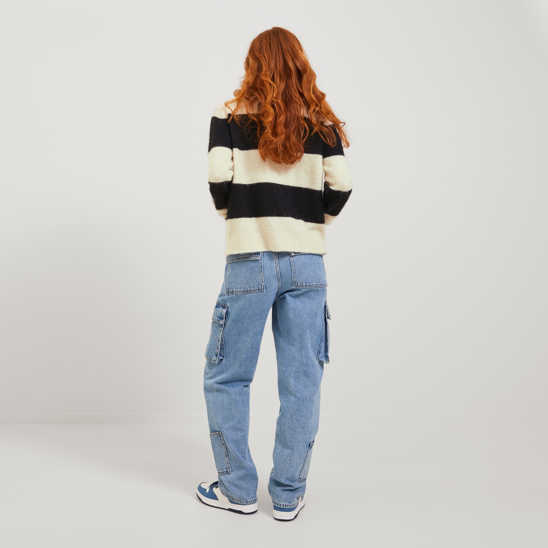 Pessoa de costas com camisola de riscas preta e bege, calças de ganga cargo azuis e ténis brancos com azul e preto