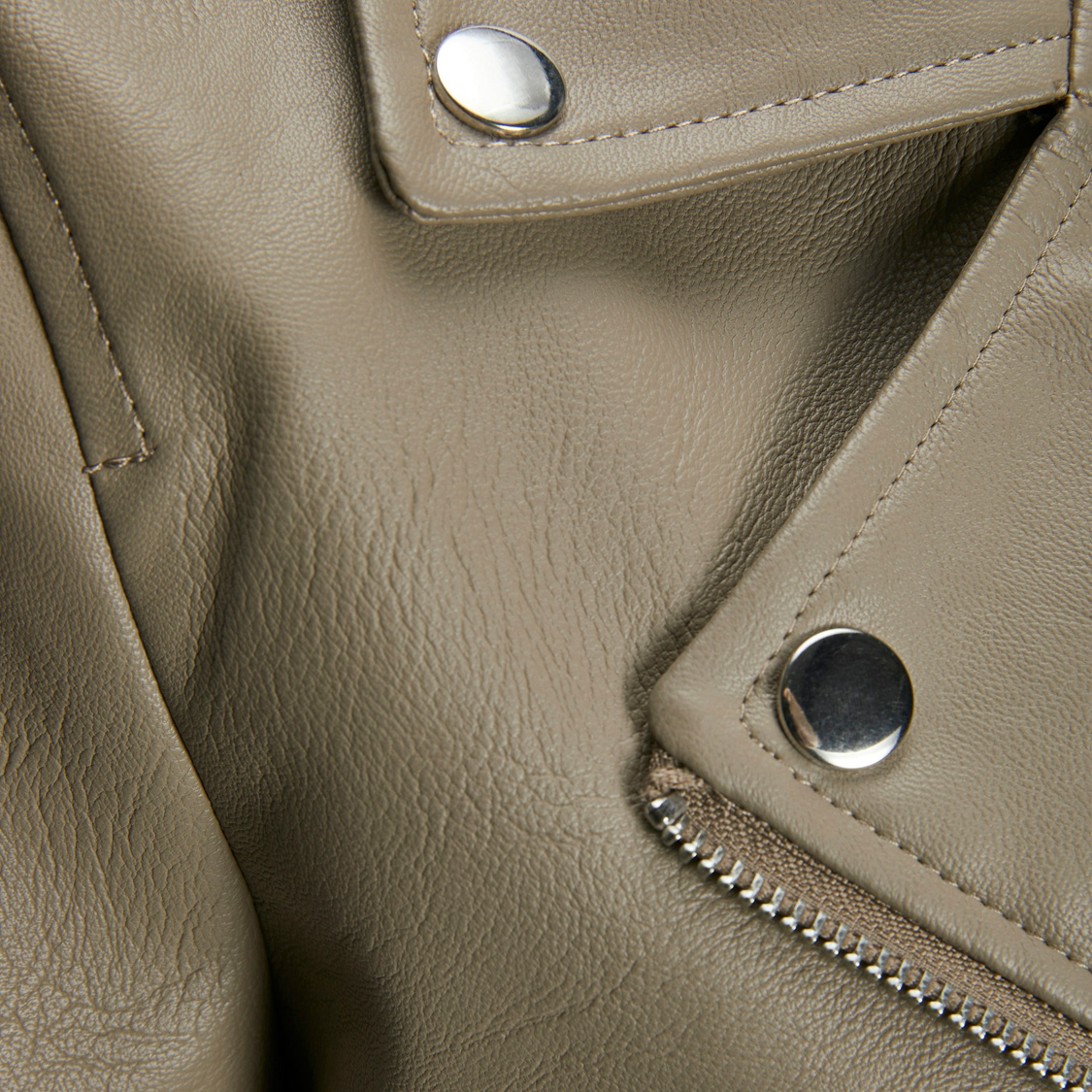 Detalhe de tecido de pele sintética bege com botões metálicos e fecho de zíper prateado