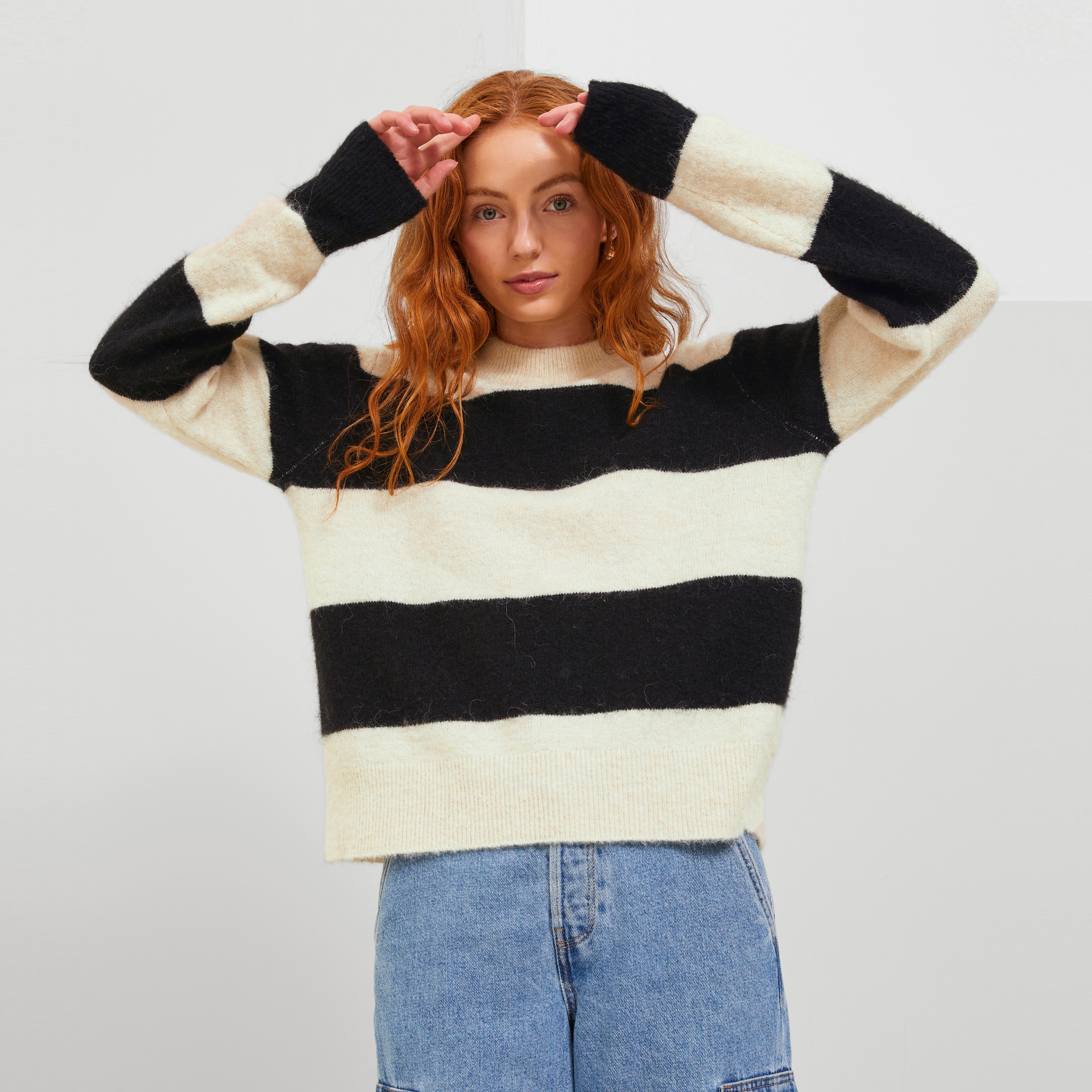 Camisola de malha riscada preta e bege com gola redonda, usada por mulher com calças de ganga azuis.