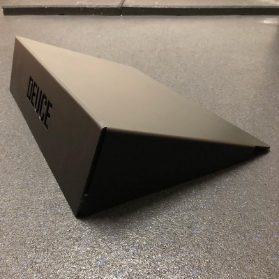 Suporte triangular preto com texto DEUCE na lateral sobre superfície cinza texturizada