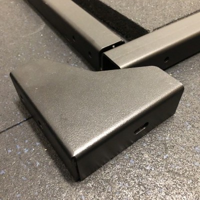 Peça metálica cinza sobre chão escuro com estrutura metálica ao fundo