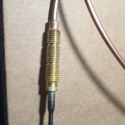 Cabo metálico com revestimento dourado e ponta preta sobre superfície bege com mola azul parcial