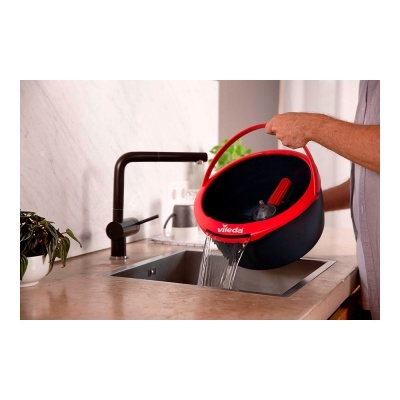 Balde Vileda preto e vermelho a ser esvaziado numa pia de cozinha com torneira preta