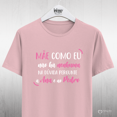 T-shirt rosa com texto colorido pendurada num cabide branco num fundo branco de parede de madeira