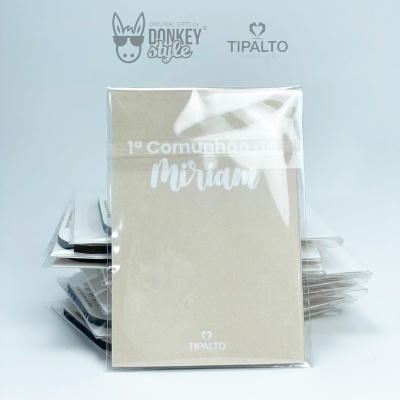 Convites de comunhão empilhados na embalagem de plástico, em bege e branco com texto e logotipos