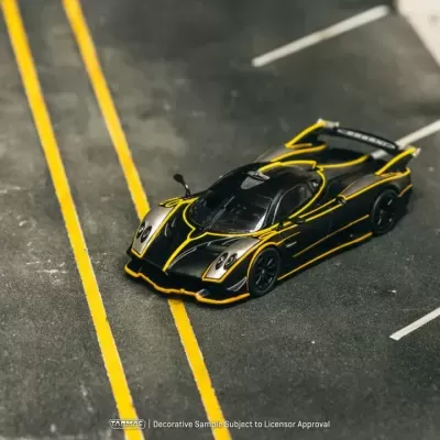 Miniatura de carro desportivo preto com detalhes em amarelo numa maquete de parque de estacionamento