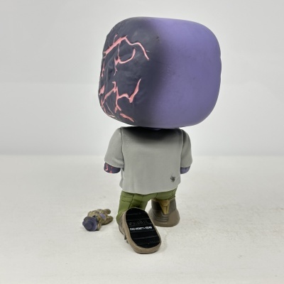 Figura Funko Pop cabeça roxa com veias cor de rosa, roupa cinza, calças verdes, botas castanhas e mão extra dourada no chão