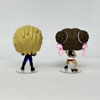 Duas figuras Funko Pop vistas de costas com cabelo loiro e castanho, roupas distintas, sobre bases transparentes