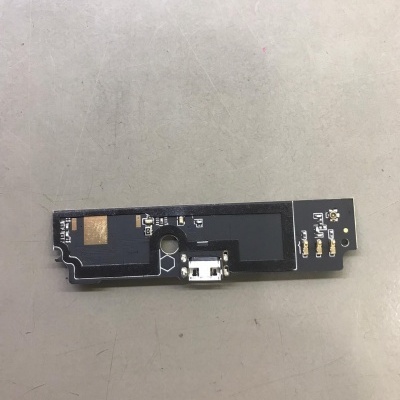 Placa eletrónica preta com conector branco num fundo cinzento.