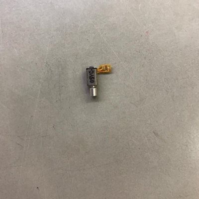 Motor vibratório pequeno com fita flexível amarelo sobre superfície cinza