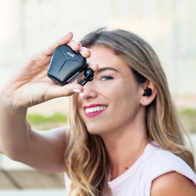 Fones de ouvido sem fios pretos com estojo de carregamento nas mãos de mulher sorridente ao ar livre