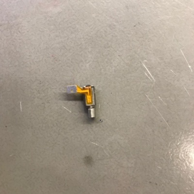 Peça eletrónica com cabo flexível amarelo e conector metálico em chão cinzento