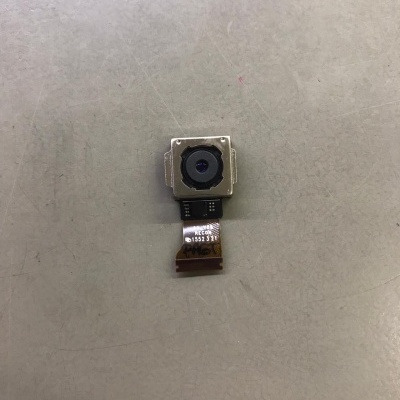 Pequena câmara de telemóvel com lente preta em estrutura metálica quadrada e fita flexível com texto visível numa superfície cinzenta.