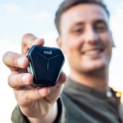 Caixa de carregamento preta com logo 'cool' em foco e pessoa sorridente ao fundo desfocado