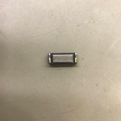 Componente electrónico retangular metálico com duas bordas douradas sobre superfície branca