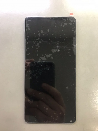 Smartphone com ecrã preto marcado por manchas e riscos sobre superfície clara