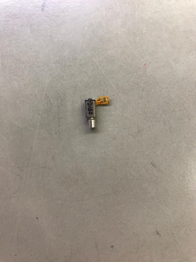 Motor vibratório pequeno com fita flexível amarelo sobre superfície cinza