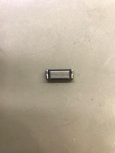 Componente electrónico retangular metálico com duas bordas douradas sobre superfície branca