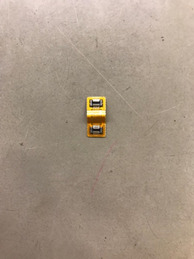 Componente eletrónico flexível amarelo com duas partes metálicas prateadas sobre superfície cinzenta