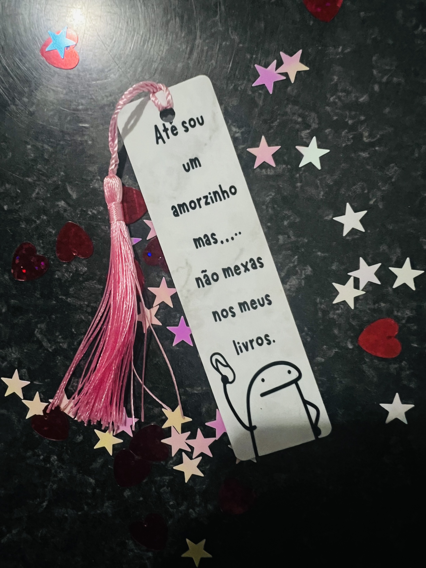 Marcador de páginas branco com tassel rosa e confetes coloridos numa superfície escura