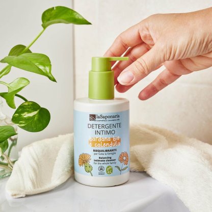 Gel higiene íntima biológico Bardana e Calêndula - La Saponaria Frasco de detergente íntimo LaSaponaria com tampa verde, toalha branca e planta verde