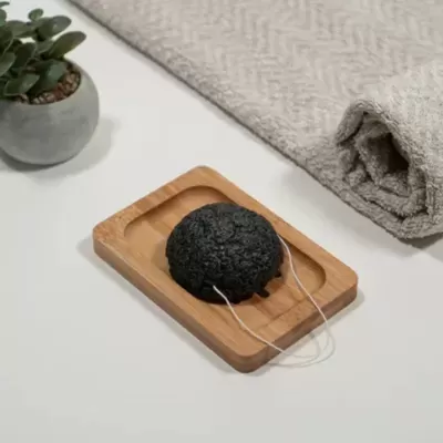 Esponja preta numa saboneteira de madeira com toalha cinzenta e planta num vaso pequeno