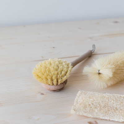 Escova de limpeza, esfregão e esponja sobre mesa de madeira clara