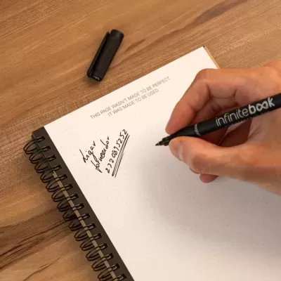 Caderno espiral com páginas pontilhadas e caneta preta escrita sobre mesa de madeira