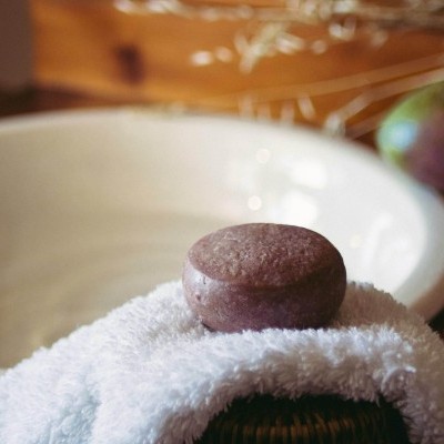 Sabonete castanho redondo sobre toalha branca felpuda com bacia creme ao fundo