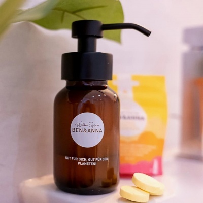 Frasco dispensador castanho com tampa preta e comprimidos amarelos ao lado