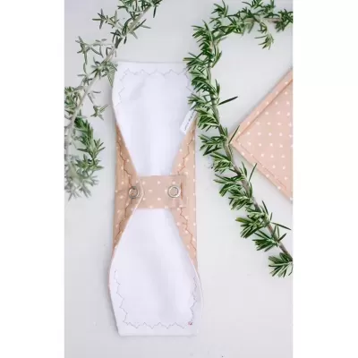 Suporte de tecido bege com bolinhas brancas e interior branco, acompanhado por ramos verdes