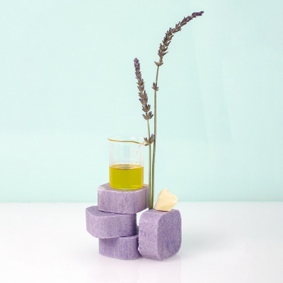 Sabonetes lilás, frasco com líquido amarelo, ramo de lavanda seco e pedra creme em fundo azul claro