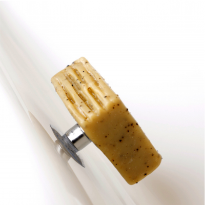 Barra esfoliante bege com partículas escuras numa superfície metálica curva