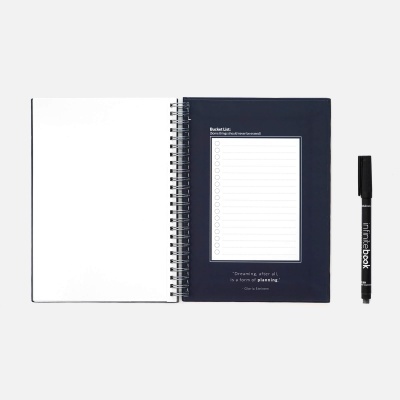 Caderno espiral aberto com capa azul e caneta preta sobre fundo branco