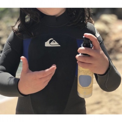 Criança com fato de neoprene preto e azul segurando embalagem amarela spray na praia