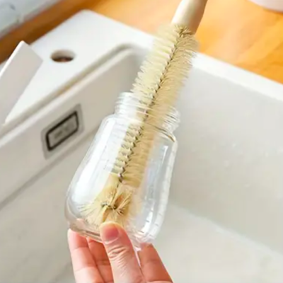 Escova de limpeza com cabo de madeira a limpar frasco de vidro transparente numa cozinha