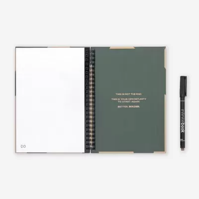 Caderno verde escuro com texto dourado, páginas pontilhadas e caneta preta