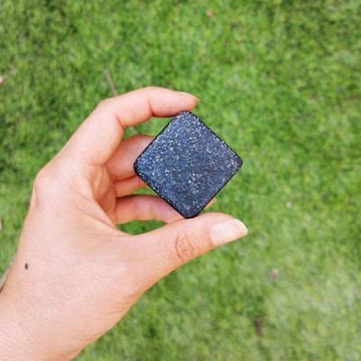 Mão segura cubo pequeno preto brilhante com partículas cintilantes sobre relva verde