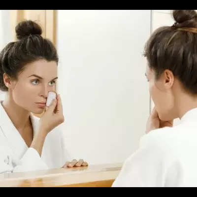 Mulher com robe aplicando produto facial junto de espelho