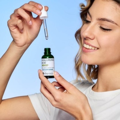 Serum facial com ácido hialurónico em frasco verde segurado por mulher sorridente