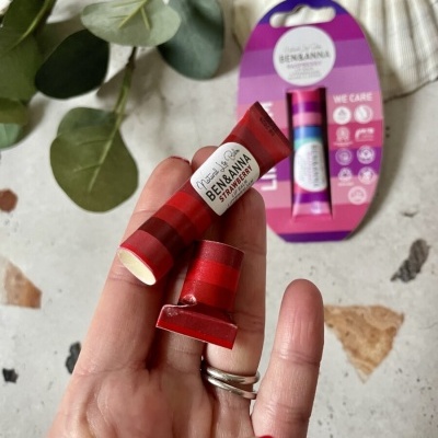 Batom labial vermelho Na! Naturals BEN & ANNA STAWBERRY numa mão com embalagem ao fundo